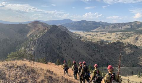 Firefighters hike down an open ridge with mountains in the background.