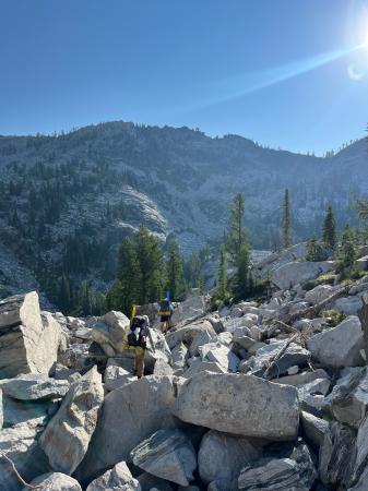 Landscape shot with mountain in background, foreground is boulder field with two people hiking